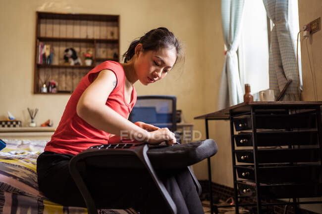 Low angle of ethnic lady sitting on bed and checking soft seat with handles while assembling chair at home — Stock Photo