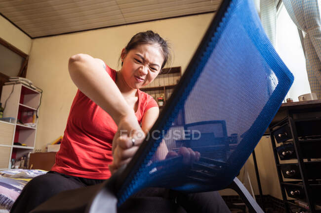 Снизу этническая женщина сидит на стуле и собирает современный новый стул в уютной спальне на дому — стоковое фото