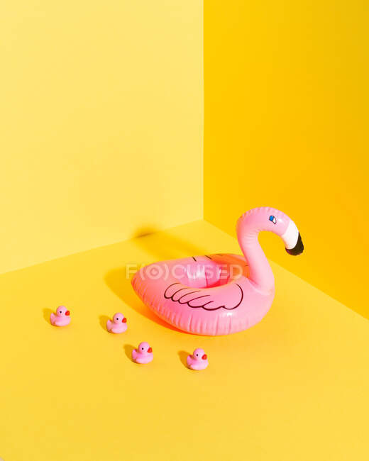 Красочная композиция с надувным буем фламинго и миниатюрными утиными игрушками на жёлтом фоне — стоковое фото