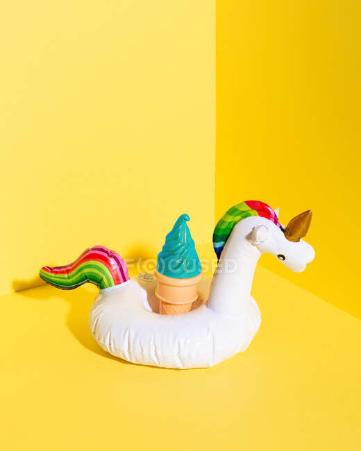 Composizione ad alto angolo con giocattolo gonfiabile unicorno e cono gelato artificiale posto sullo sfondo giallo — Foto stock