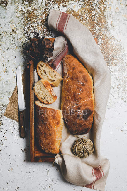 From above rustic composition with aromatic bread loaves on board with linen towel and knife on shabby surface — Stock Photo
