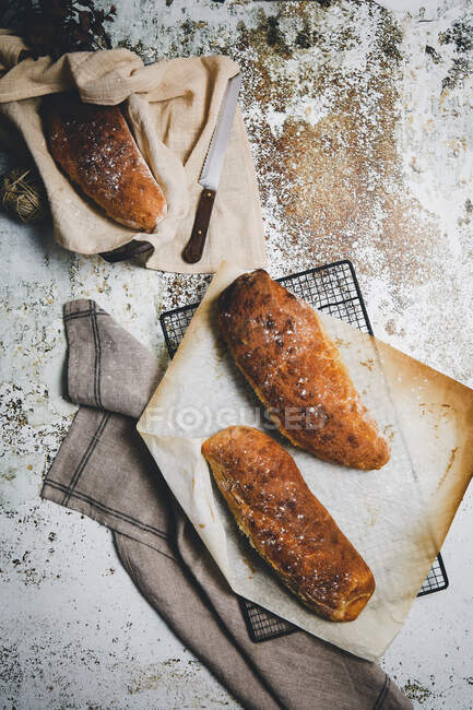 Сверху деревенский состав с ароматическими хлебами на борту с льняным полотенцем и ножом на потрепанной поверхности — стоковое фото