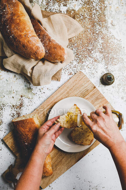 Blick von oben auf die Person, die Bio-Olivenöl auf geschnittene Scheiben frisches Brot gießt — Stockfoto