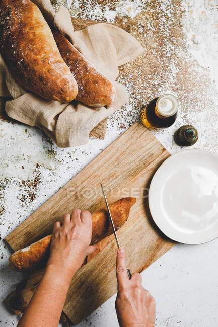 Dall'alto di cuoco che taglia il pane al forno d'oro su asse di legno su superficie rustica — Foto stock