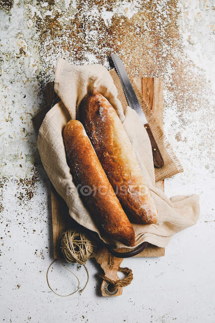 Сверху деревенский состав с ароматическими хлебами на борту с льняным полотенцем и ножом на потрепанной поверхности — стоковое фото