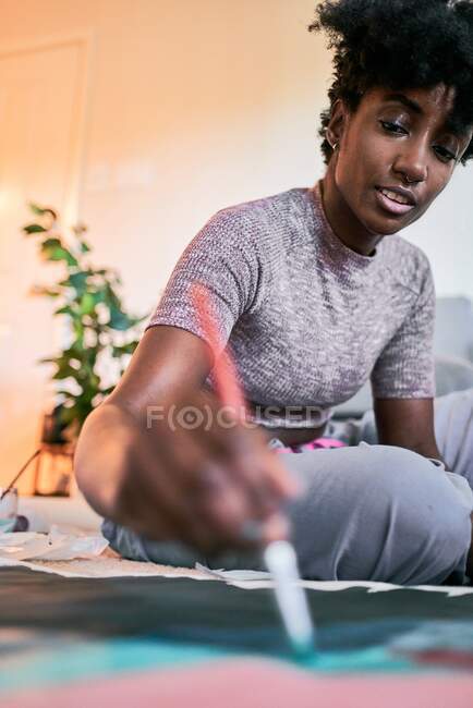 Von oben der Ernte anonyme schwarze Frau mit Pinsel Zeichnung bunte Bild auf Papier, während auf dem Boden zu Hause sitzen — Stockfoto