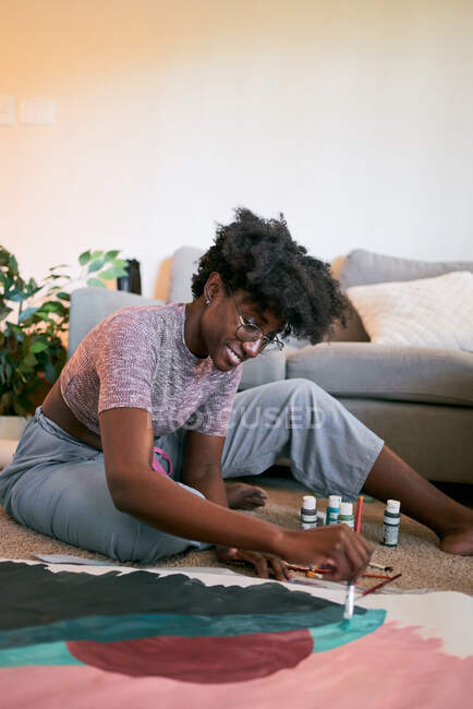 Von oben der Ernte anonyme schwarze Frau mit Pinsel Zeichnung bunte Bild auf Papier, während auf dem Boden zu Hause sitzen — Stockfoto