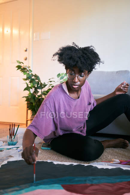 De cima da colheita fêmea preta anônima com desenho pincel imagem colorida no papel enquanto sentado no chão em casa — Fotografia de Stock