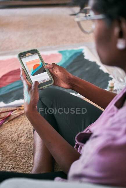 De cima da colheita fêmea preta anônima com desenho pincel imagem colorida no papel enquanto sentado no chão em casa — Fotografia de Stock