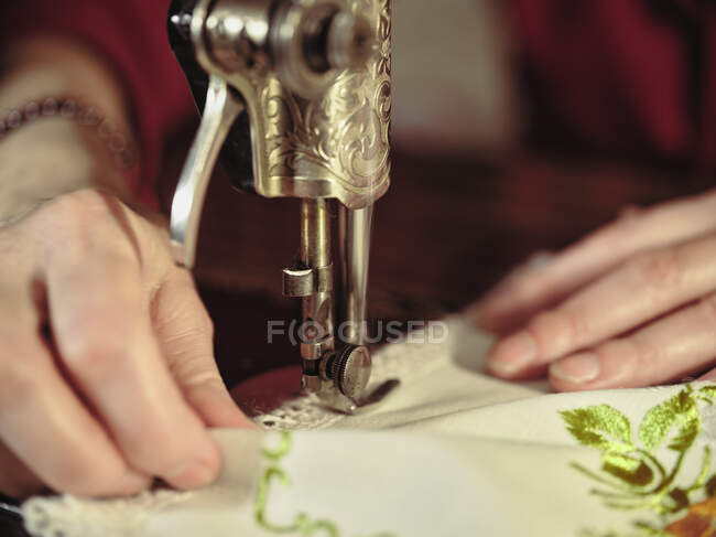 Senior senhora em óculos usando máquina de costura retro para criar guardanapo de linho no quarto acolhedor em casa — Fotografia de Stock