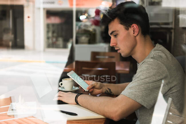 Male freelancer using laptop and smartphone in cafeteria — Stock Photo