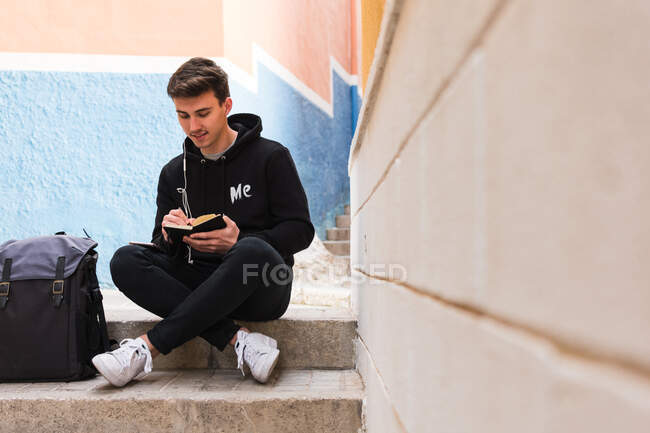 Студент-мужчина делает заметки на улице — стоковое фото
