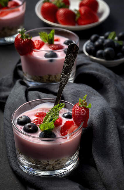 Hausgemachter Joghurt mit Erdbeeren, Blaubeeren und Müsli mit dunklem Hintergrund und Sonnenlicht. Gesundes Ernährungskonzept. Veganes Essen — Stockfoto