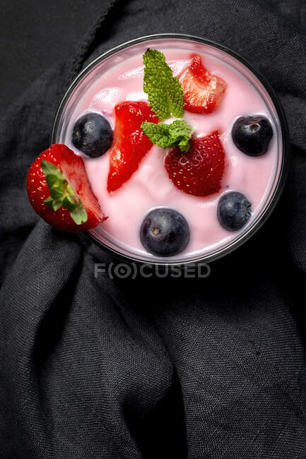 Домашний йогурт с клубникой, черникой и злаками сверху с темным фоном и солнечным светом. — стоковое фото