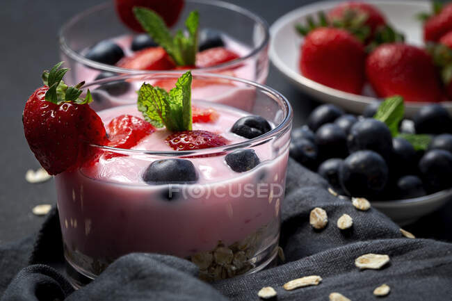 Hausgemachter Joghurt mit Erdbeeren, Blaubeeren und Müsli mit dunklem Hintergrund und Sonnenlicht. Gesundes Ernährungskonzept. Veganes Essen — Stockfoto