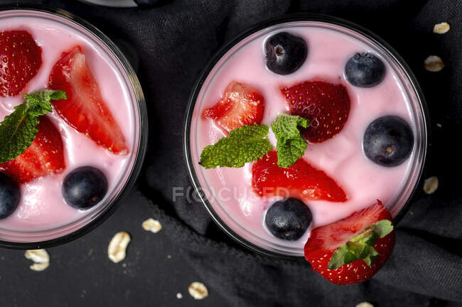 Домашний йогурт с клубникой, черникой и злаками с темным фоном и солнечным светом. — стоковое фото