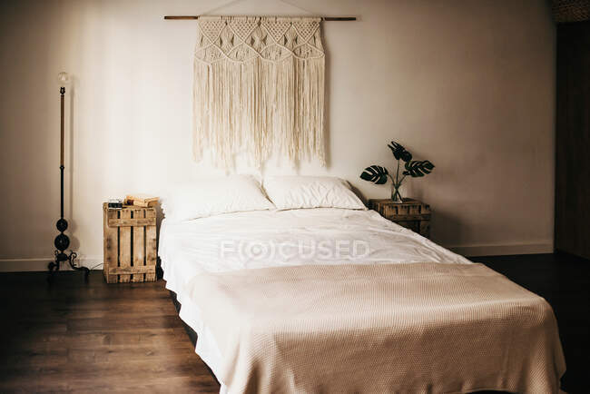Винтажное украшение макраме висит на стене над удобной кроватью в уютной спальне дома — стоковое фото