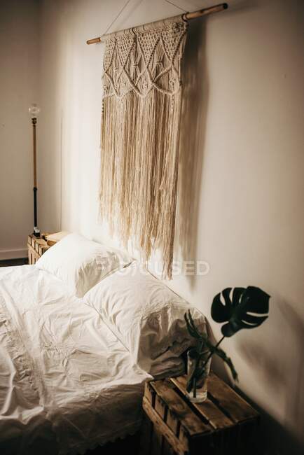Vintage Makramee Dekoration hängt an der Wand über bequemem Bett im gemütlichen Schlafzimmer zu Hause — Stockfoto