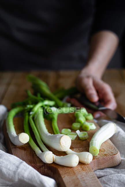 Cropped woman hands with knife and bunch of ripe scallions placed on wooden cutting board and cloth napkin on rustic table in kitchen — Stock Photo