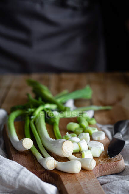 Bunch of ripe scallions placed on wooden cutting board and cloth napkin on rustic table in kitchen — Stock Photo