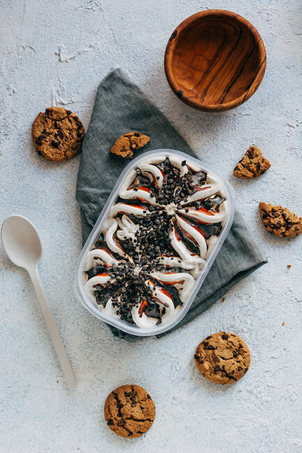 Top view of oatmeal cookies plastic container of ice cream placed on napkin near spoon and bowl on stucco surface — Stock Photo