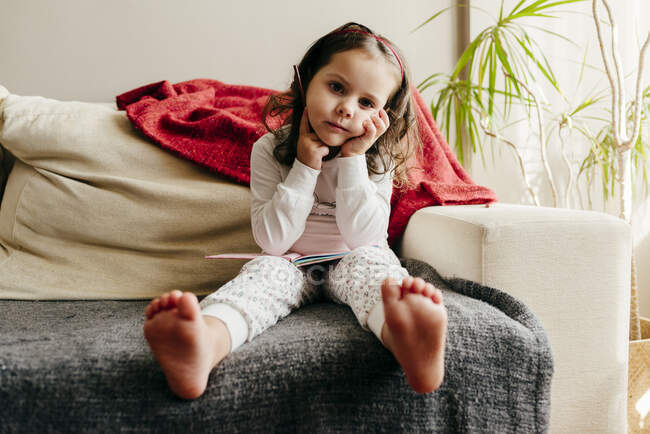 Menina bonito sentado no sofá com um caderno à procura de inspiração — Fotografia de Stock