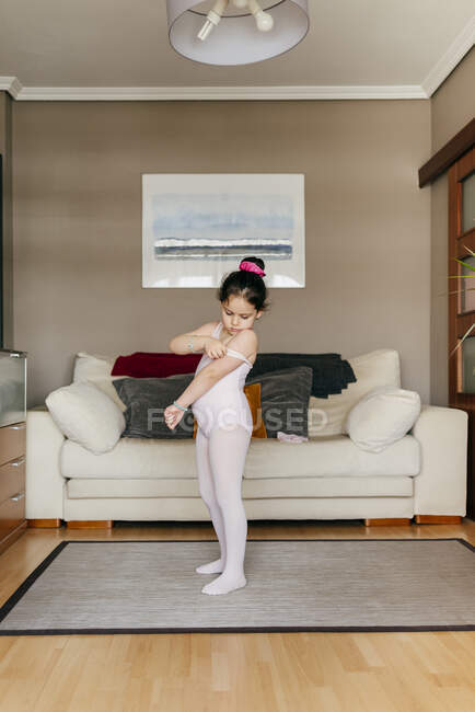 Cute little girl in light pink leotard and tights getting ready while standing near dance shoes in cozy living room at home — Stock Photo