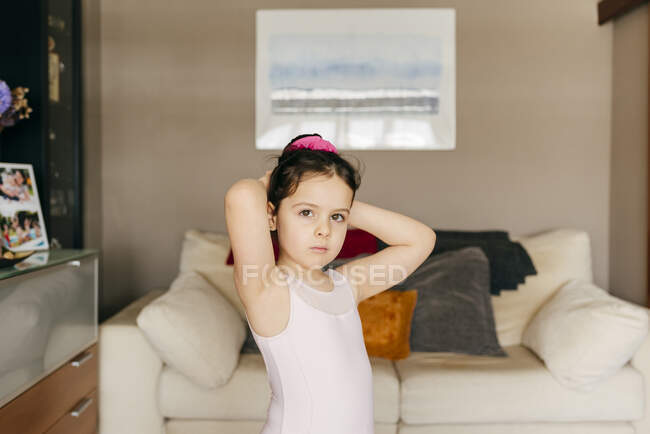Adorable upset little girl dancer in leotard looking away while doing hair bun before ballet training in cozy living room at home — Stock Photo
