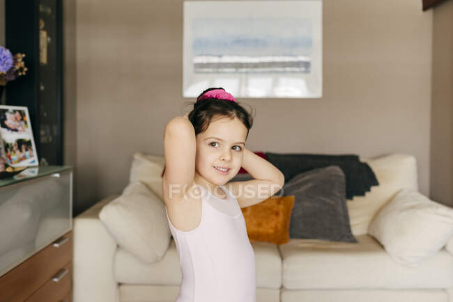 Чарівна щаслива маленька дівчинка танцівниця в леопарді, дивлячись геть, роблячи зачіску до тренування балету в затишній вітальні вдома — стокове фото