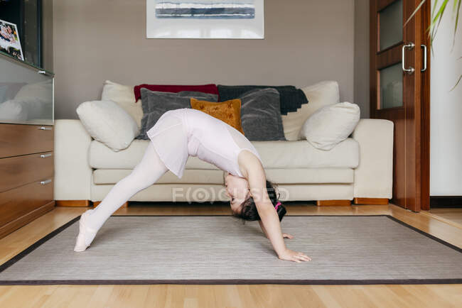 Vista laterale della bambina in body che fa esercizio sul pavimento durante le prove di danza a casa — Foto stock