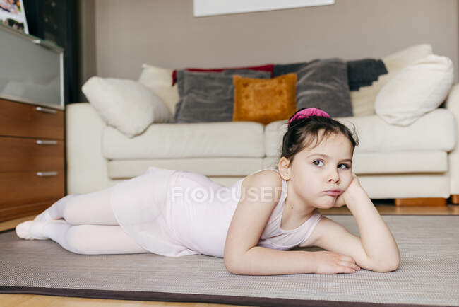 Ennuyé petite fille réfléchie en justaucorps couché sur le sol regardant loin tout en se reposant pendant la répétition de ballet à la maison — Photo de stock