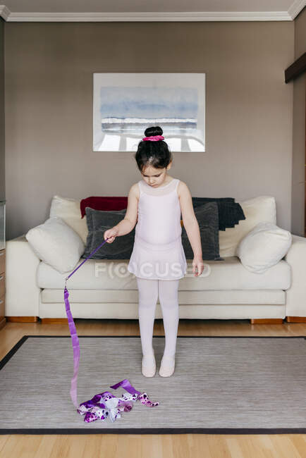 Focused cute little girl in leotard and tights spinning ribbon during rhythmic gymnastic practice training in cozy living room at home — Stock Photo