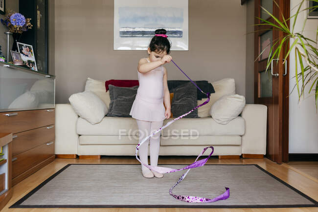 Enfocado linda niña morena en maillot y medias, mientras que la cinta giratoria durante el entrenamiento de práctica gimnástica rítmica en acogedora sala de estar en casa - foto de stock