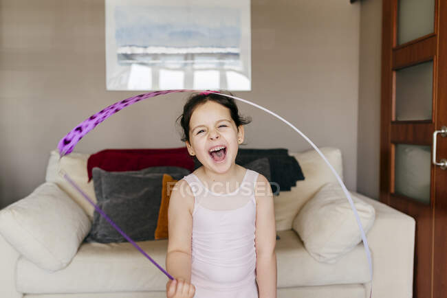 Jolie petite fille brune heureuse avec ruban aux yeux fermés pendant l'entraînement gymnastique rythmique à la maison — Photo de stock