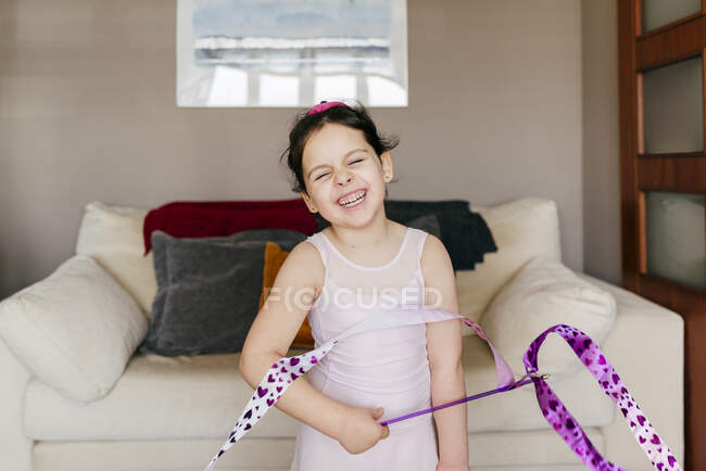 Linda niña morena feliz con cinta con los ojos cerrados durante el entrenamiento gimnástico rítmico en casa - foto de stock