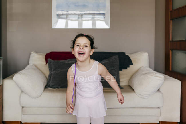 Carino felice bambina bruna con nastro sorridente guardando la fotocamera durante l'allenamento ginnico ritmico a casa — Foto stock