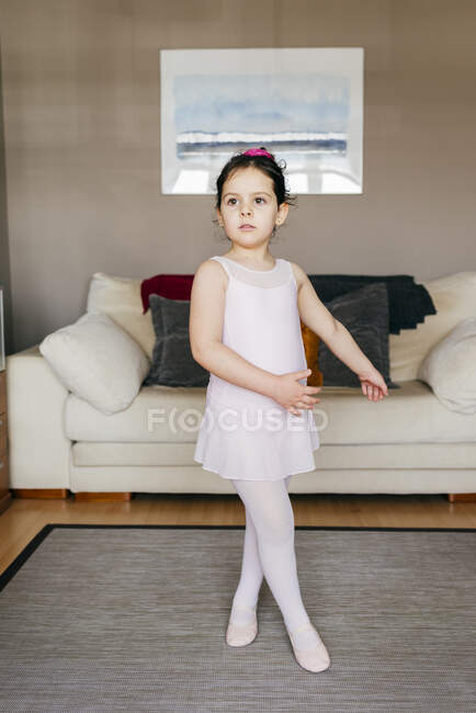 Menina bonito olhando para longe dançando perto do sofá durante o ensaio de balé em casa — Fotografia de Stock