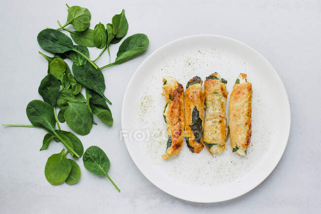 Vista superior de rolos gostosos de filé de frango assado colocado na placa perto de folhas de espinafre frescas na mesa cinza claro — Fotografia de Stock
