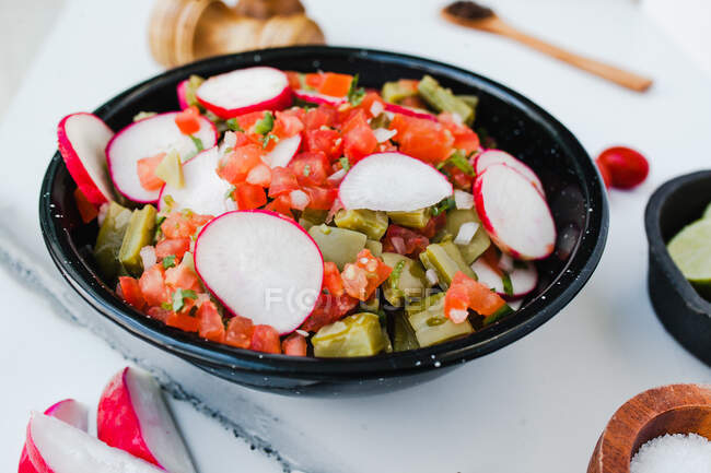 Closeup of black bowl with chopped pepper and tomatoes garnished with slices of red radish — Stock Photo