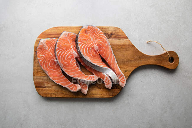 Vista superior de filetes de salmón fresco en tablero de madera preparado para deliciosa receta saludable colocada en la mesa de mármol - foto de stock
