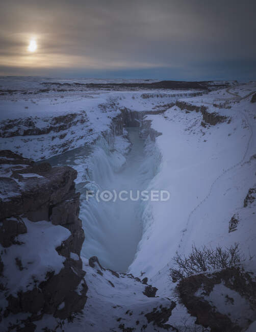 Freddo scenario nordico di terreno roccioso innevato con grande burrone sotto il cielo grigio con sole splendente attraverso le nuvole nella giornata invernale in Islanda — Foto stock