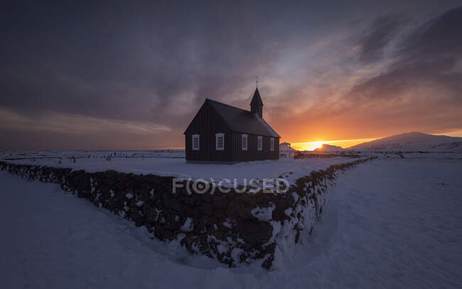 Tolle Nordkulisse mit kleiner Kirche in schneebedecktem Gelände vor bedecktem Abendhimmel bei Sonnenuntergang in Island — Stockfoto