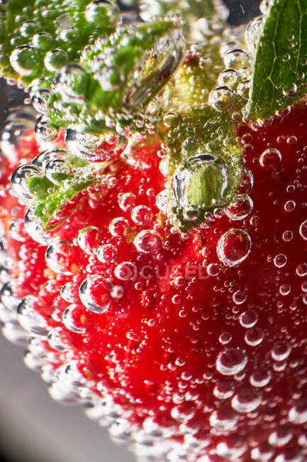 Closeup ripe red strawberry covered with air bubbles floating in transparent clear water — Stock Photo