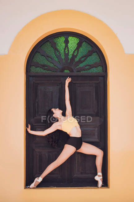 Полнотелая стройная женщина в пуантах поднимает руку, танцуя балет у декоративной двери классического здания — стоковое фото