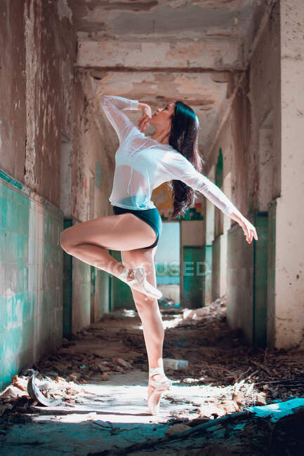 Seitenansicht einer schlanken Frau, die anmutig aufblickt und im schäbigen Flur eines verlassenen Gebäudes tanzt — Stockfoto