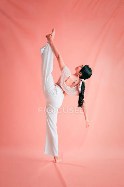 Vue arrière de la femme mince en tenue blanche faisant des fentes tout en dansant gracieusement sur fond rose — Photo de stock