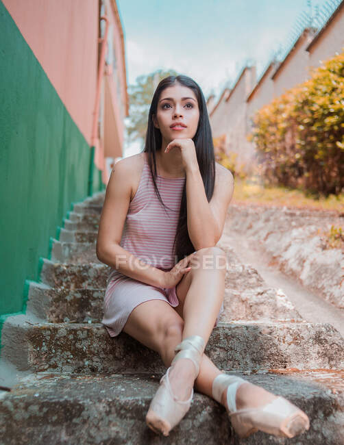 Молода брюнетка балерина в взутті сидить на похмурих сходах і відпочиває після тренувань проти смугастої стіни на вулиці — стокове фото