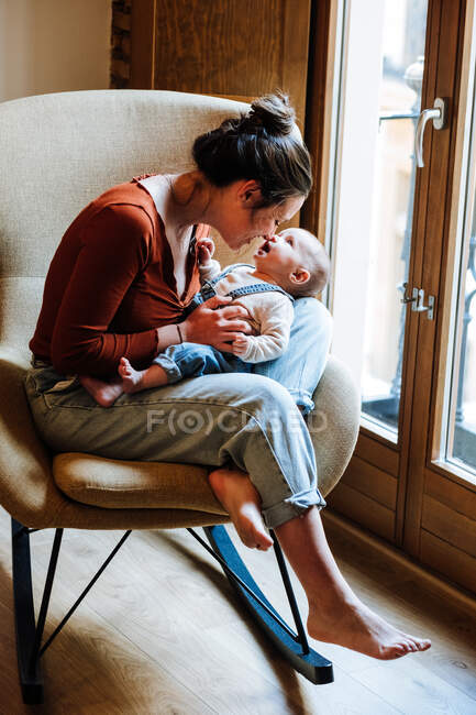 Madre con el bebé sentado cerca de la ventana - foto de stock