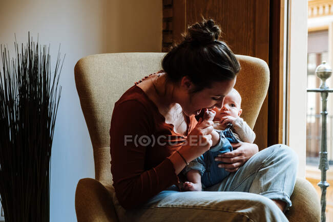 Madre con el bebé sentado cerca de la ventana - foto de stock