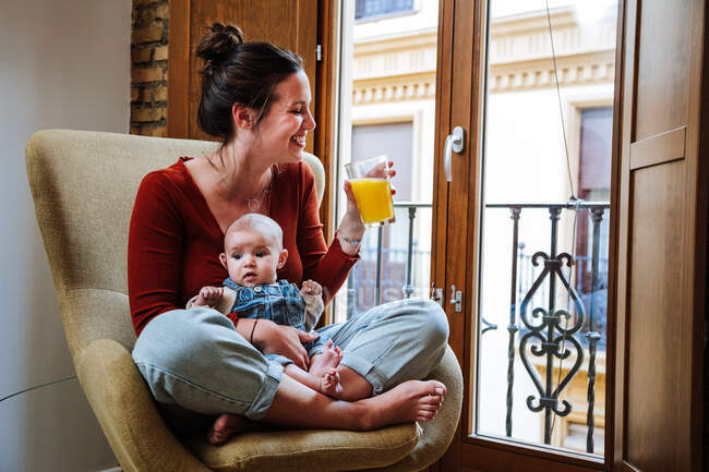 Crop mother with juice and baby resting on chair — Stock Photo
